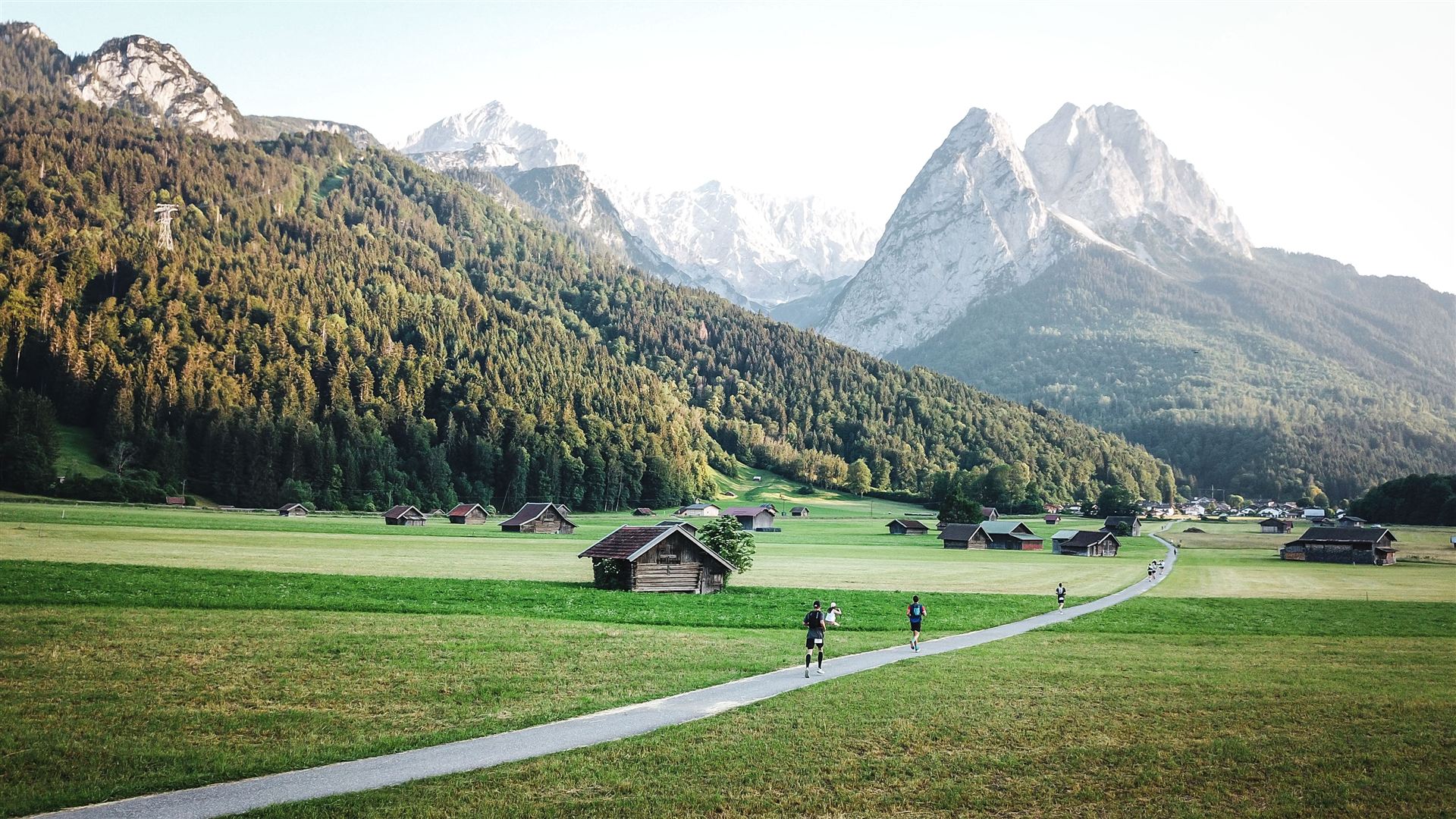 Runners on a narrow farm path beneath the Zugspitze massif at dawn